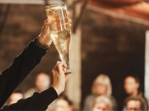Picture of a person holding a bottle of sparkling wine upside down and up to the light